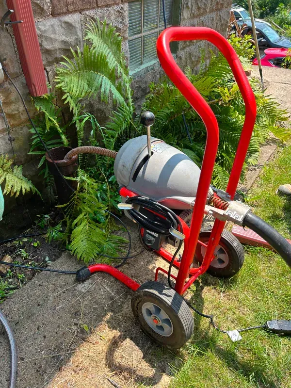 A red drain cleaner is sitting on the sidewalk in front of a house.