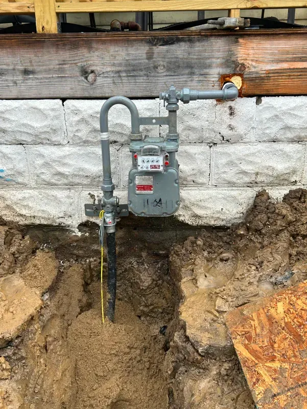 A gas meter is sitting in the dirt next to a brick wall.