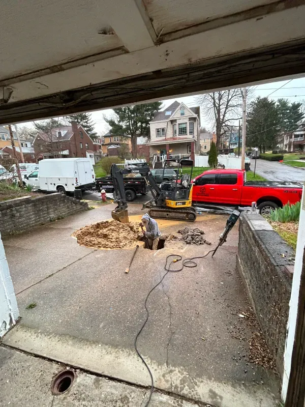 A man is digging a hole in the ground in a driveway next to a red truck.