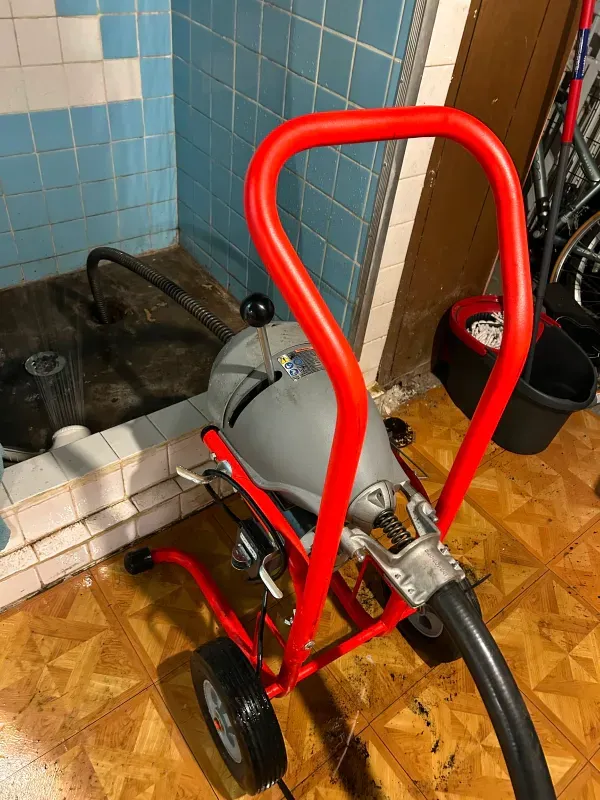 A red and gray drain cleaner is sitting on a wooden floor in a bathroom.