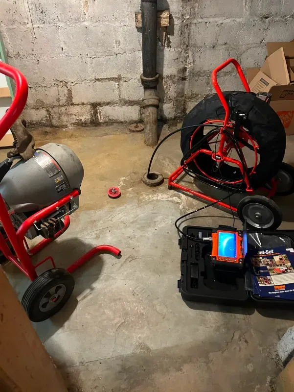 A drain cleaner and a camera are sitting on the floor in a basement.