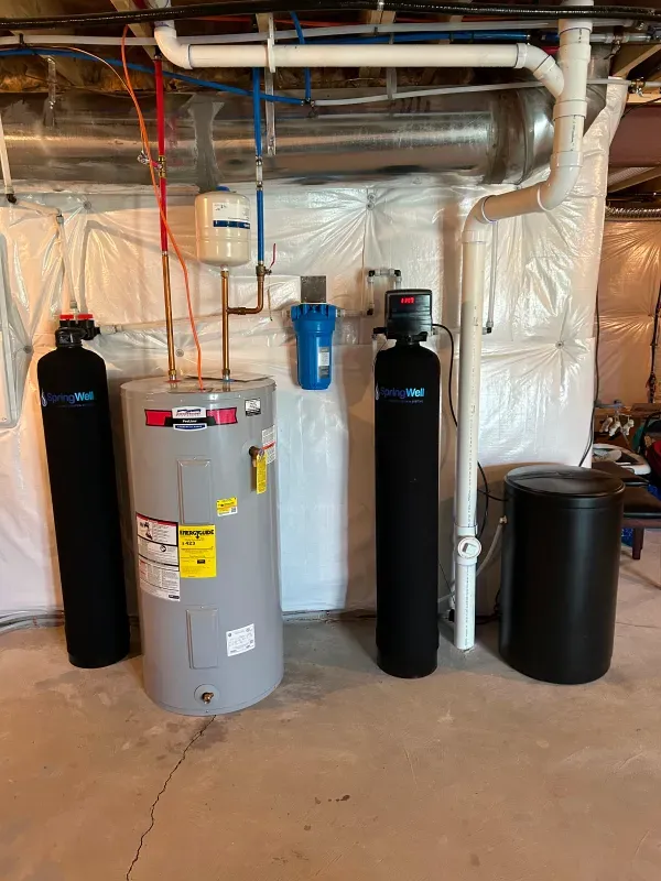 A water heater and two water filters are sitting in a basement.