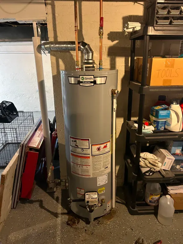 A water heater is sitting in a garage next to a shelf.