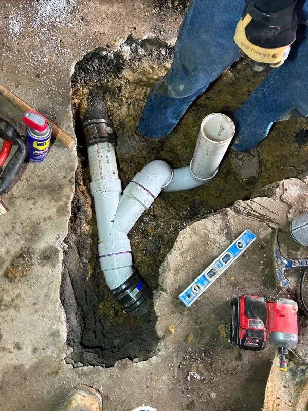 A person is working on a pipe in a hole in the ground.