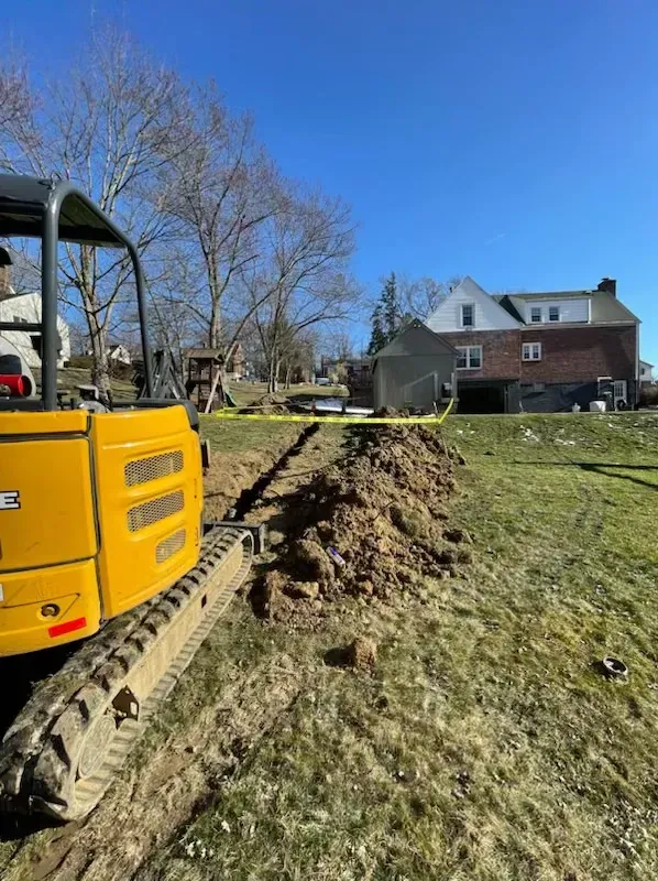 A yellow excavator is digging a hole in a yard in front of a house.