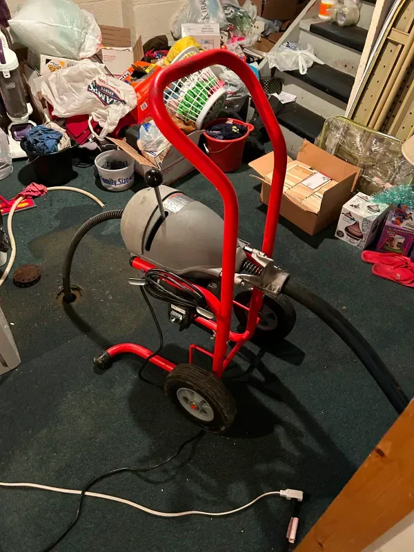 A drain cleaner is sitting on the floor in a messy room.