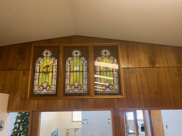 Three stained glass windows are hanging on a wooden wall