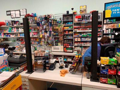 A man is behind a counter in a store with a marlboro sign on the wall.