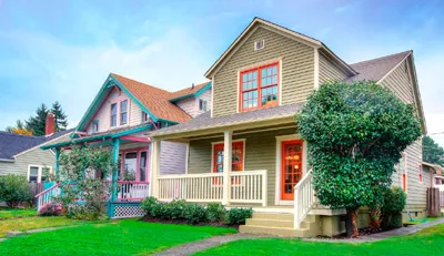 Two-story suburban house with beige siding, red trim, a porch, and a green lawn.