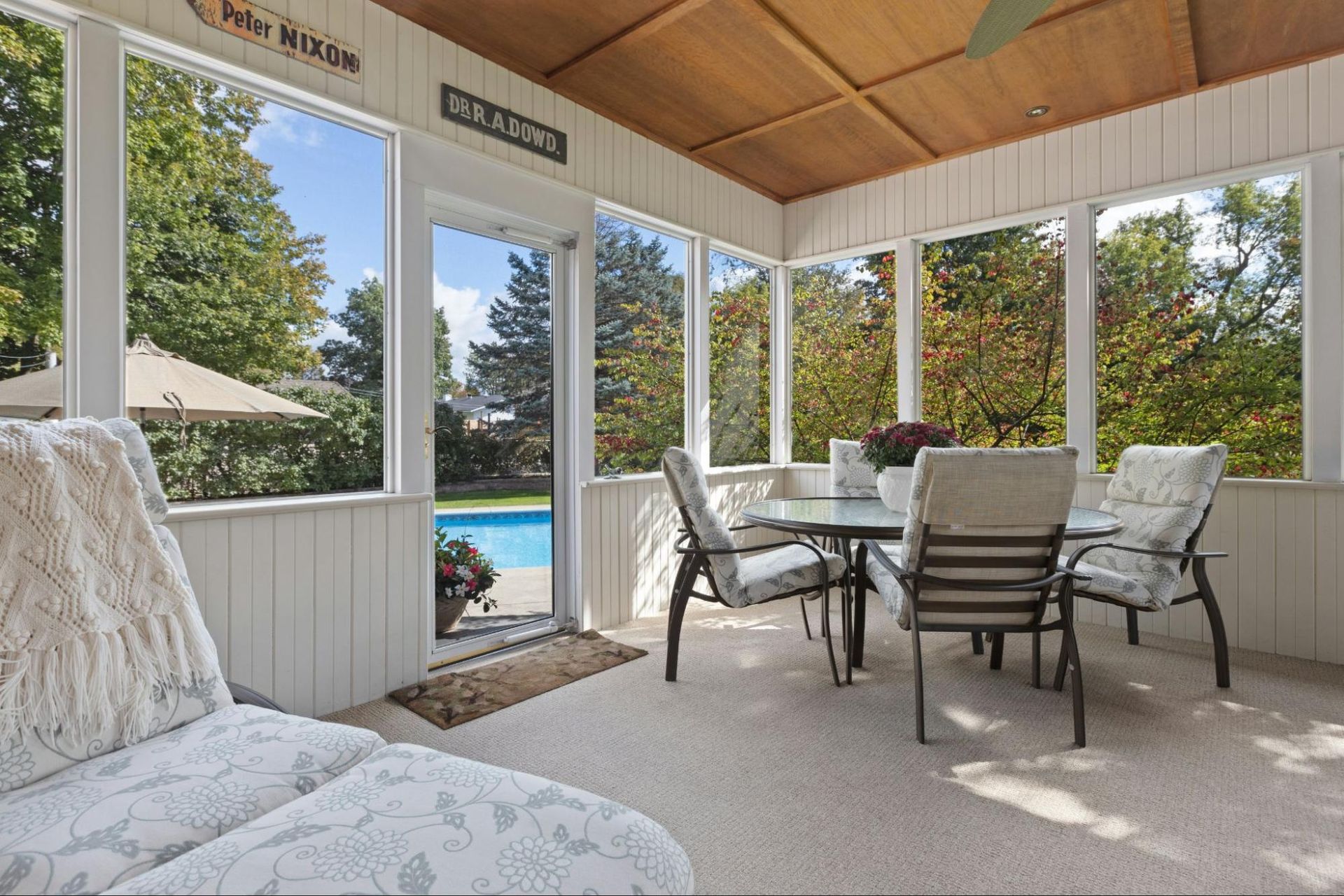 A screened in porch with a table and chairs and a pool in the background.