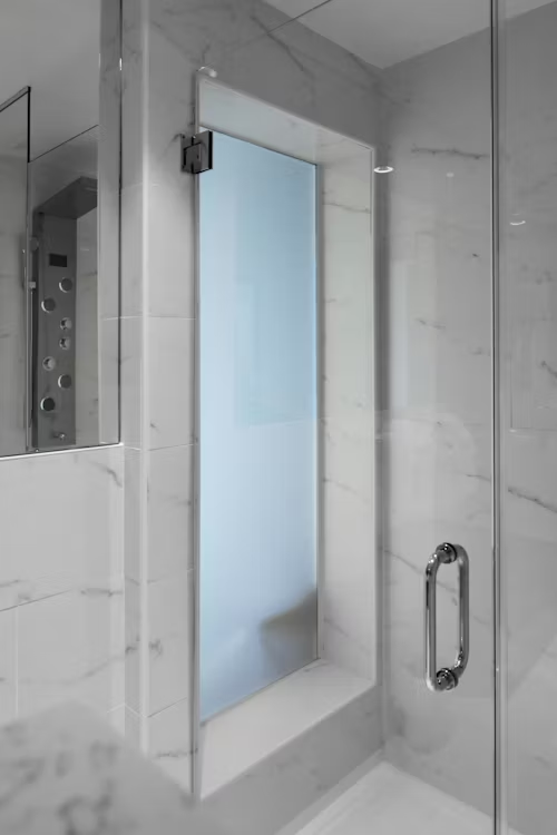 Glass shower enclosure with white marble tile and chrome handle in a bathroom