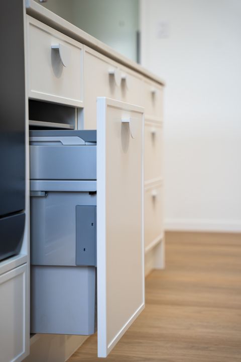 Cream-colored cabinetry with a drawer open, revealing a printer within. Light wood flooring in the background.