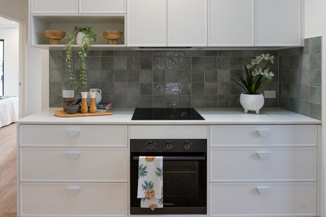 White kitchen with dark oven, backsplash tile, and countertop. Plants and decorations.
