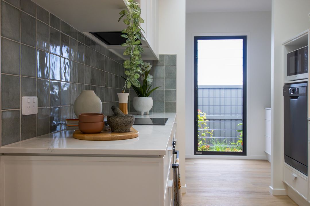 White kitchen with gray tile backsplash, countertop with decor, window to backyard.