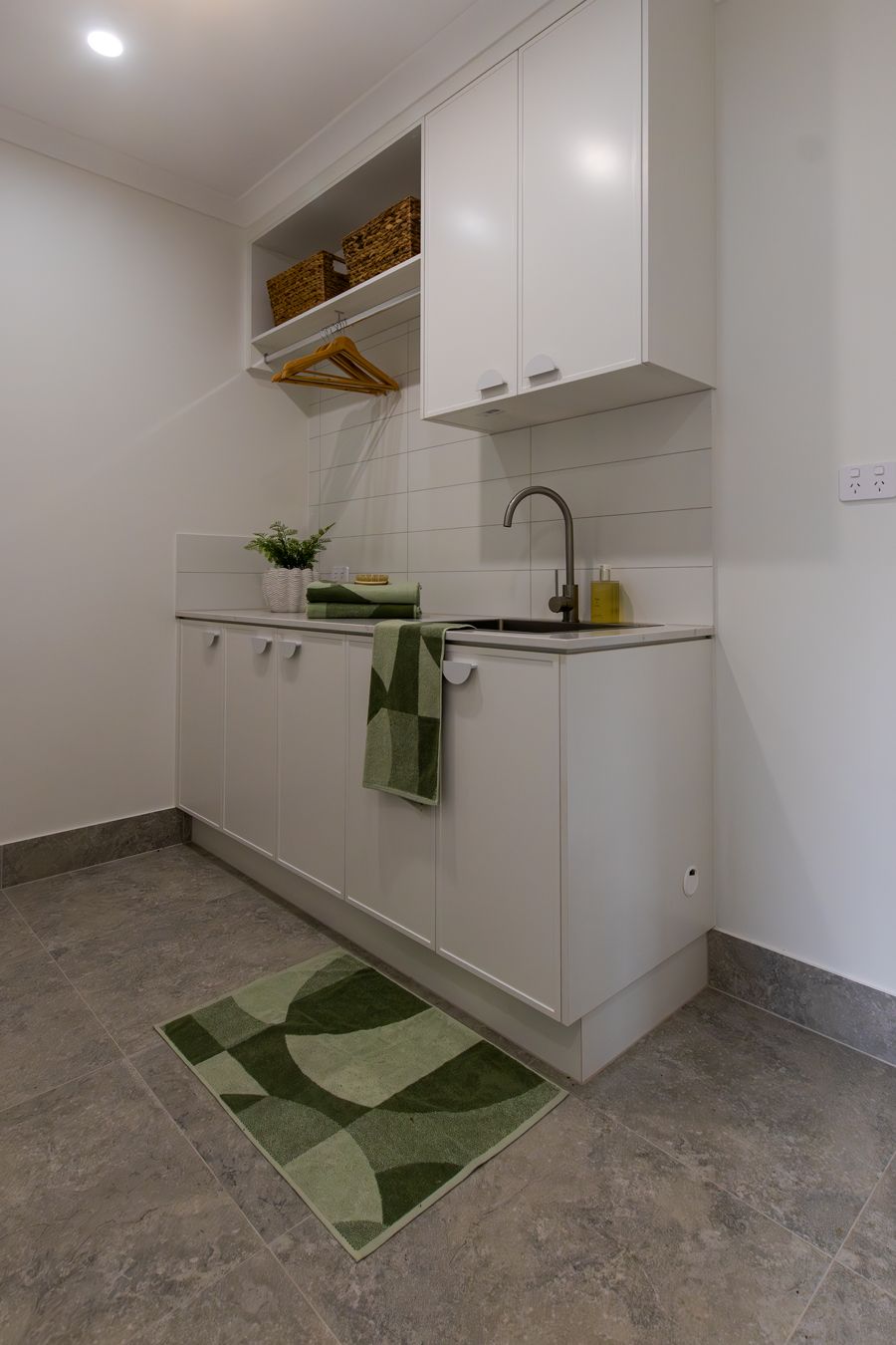 White laundry room with sink, cabinets, and green rug.