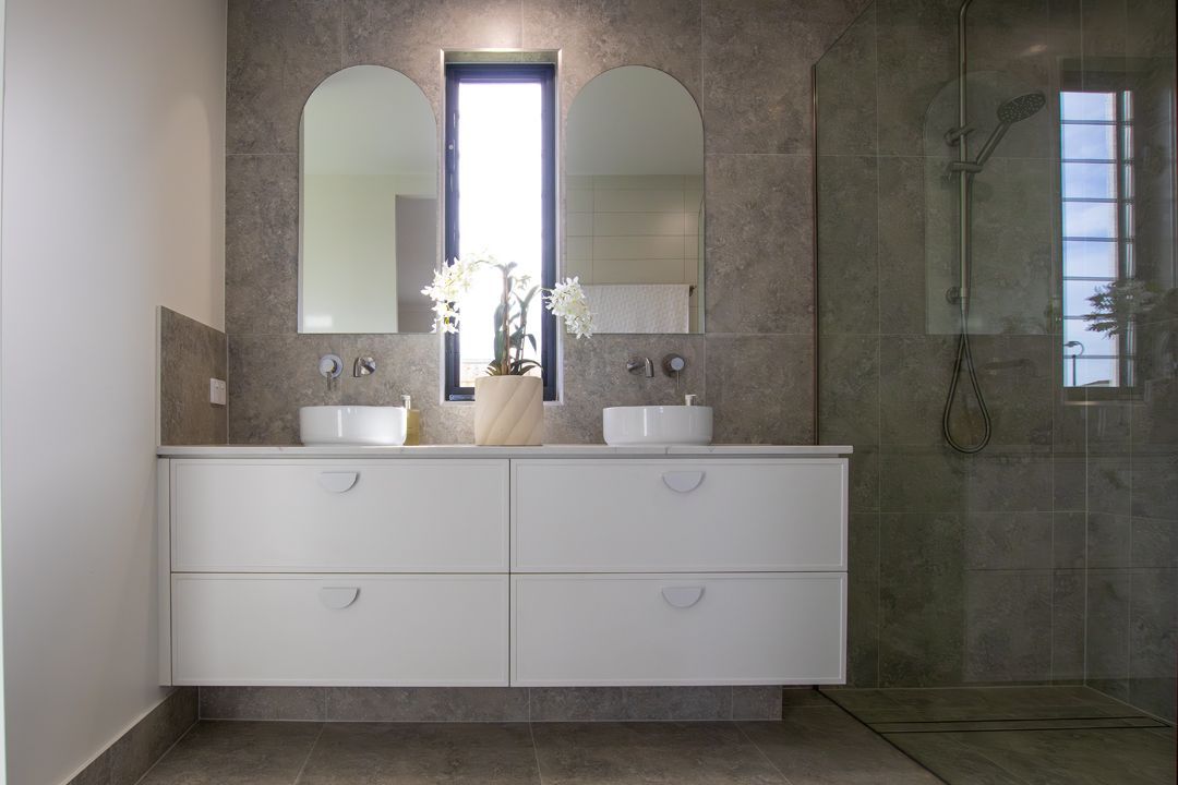 Modern bathroom with white floating vanity, arched mirrors, and gray tile.