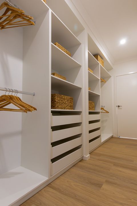 White walk-in closet with shelves, drawers, and hanging space. Wooden hangers and woven baskets on shelves. Light wood flooring.