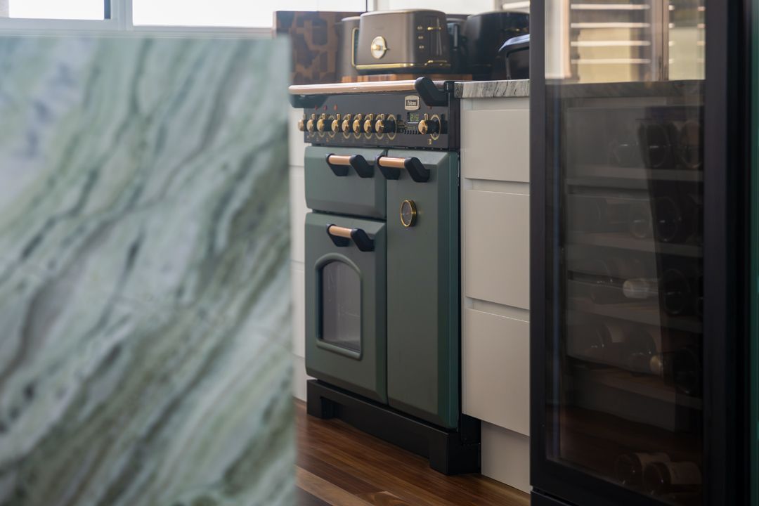 Green stove in a kitchen, next to a wine fridge and marble counter.