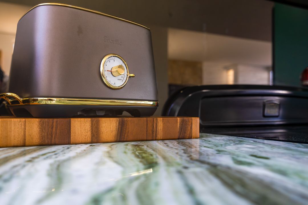 Grey toaster with gold trim and dial on a marble countertop with a wooden cutting board.