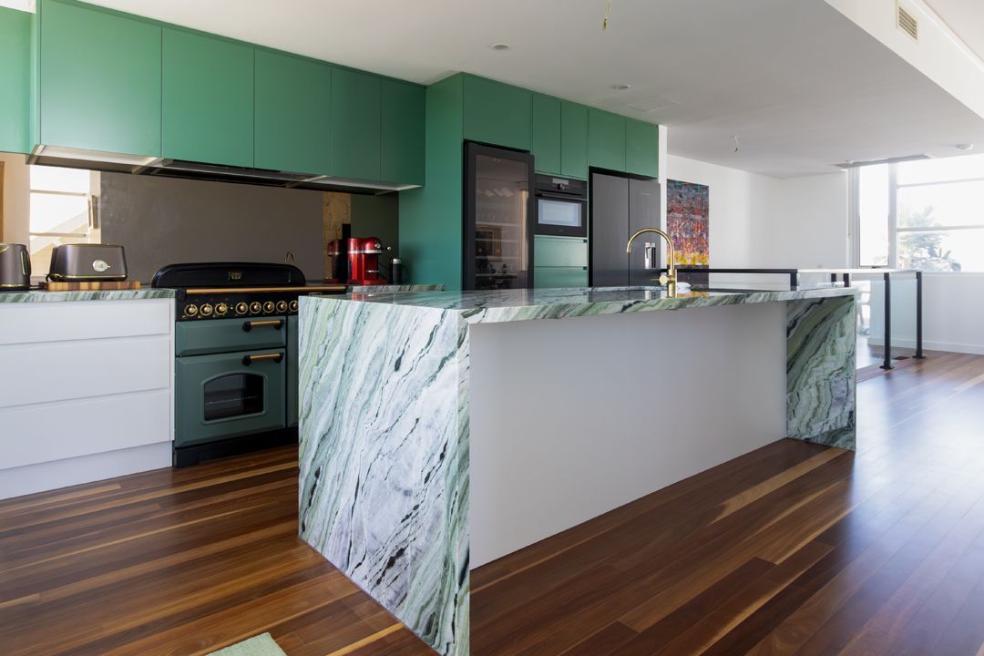 Green marble kitchen island and cabinets in a modern kitchen with wooden floors.