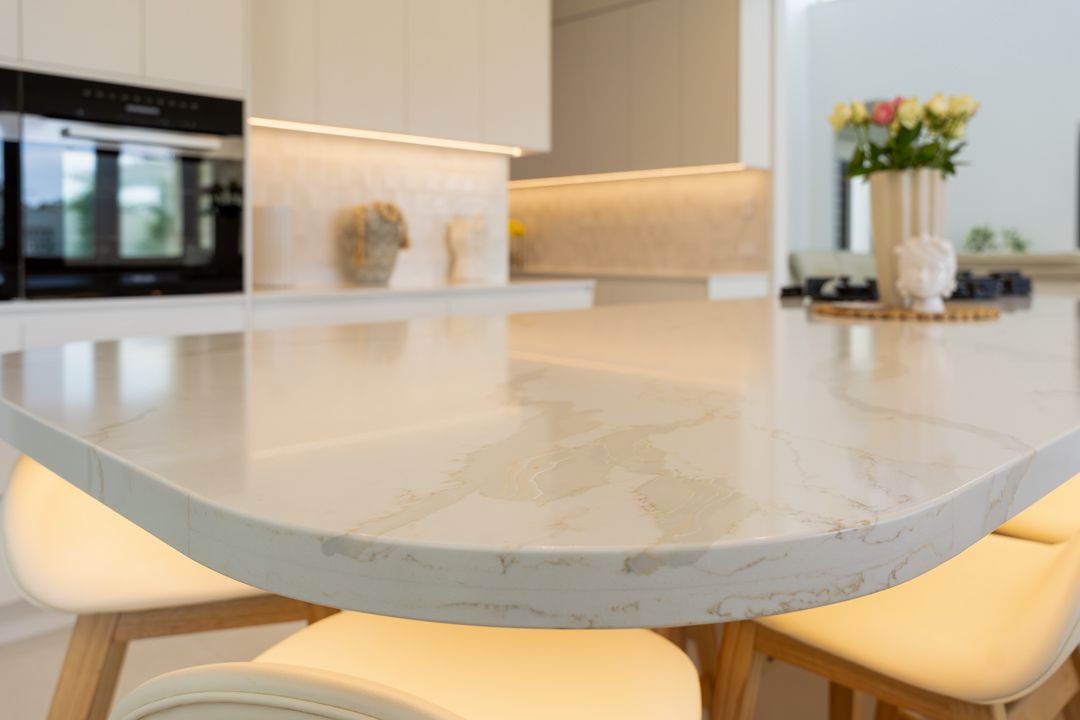 Close-up of a kitchen island with beige countertop and bar stools. White and light-colored cabinets in the background.