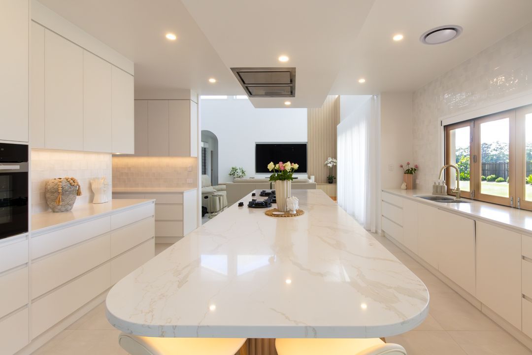 Bright white modern kitchen with marble island, cabinets, and recessed lighting. View to living room.