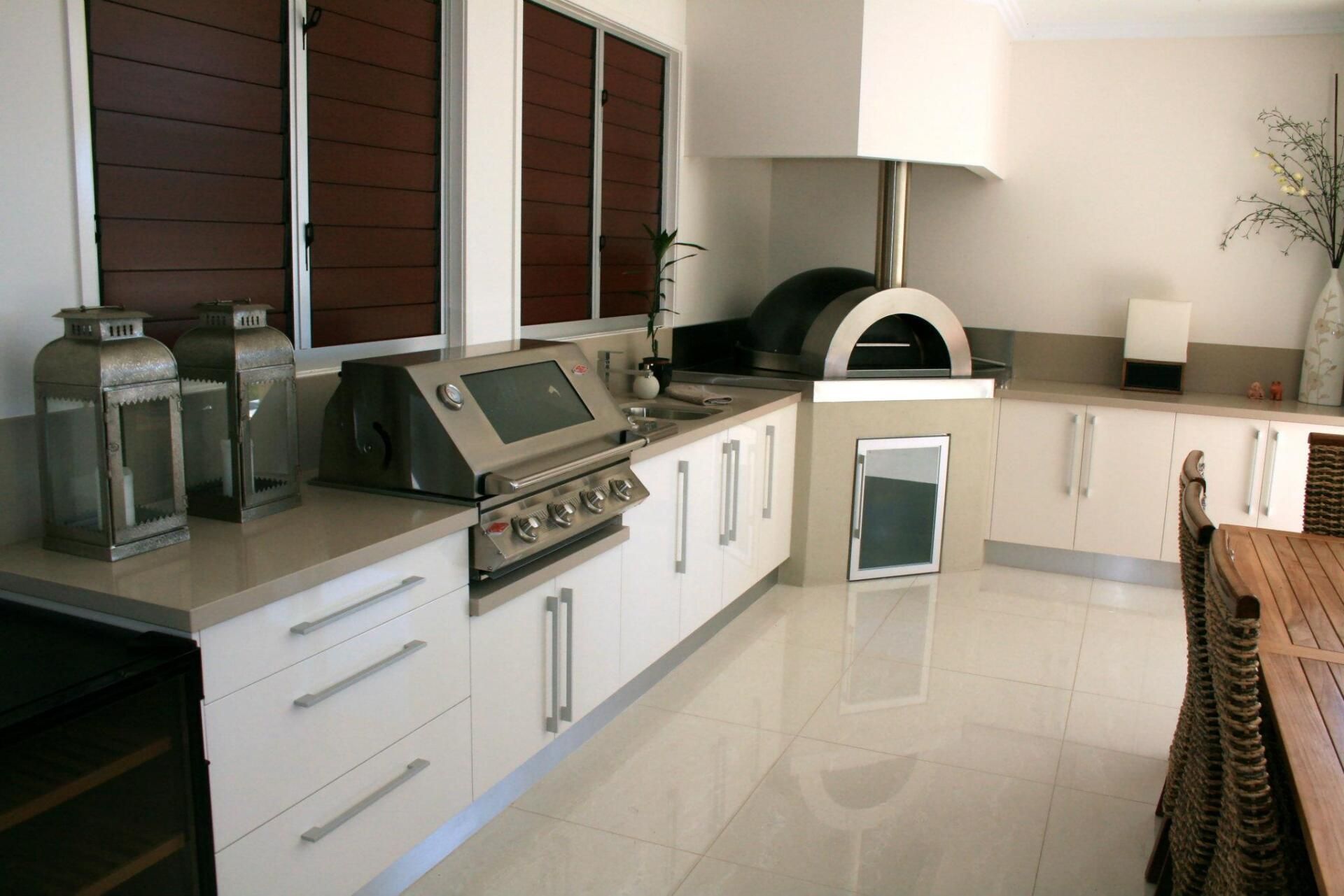 Outdoor kitchen with stainless steel grill, pizza oven, and white cabinets.