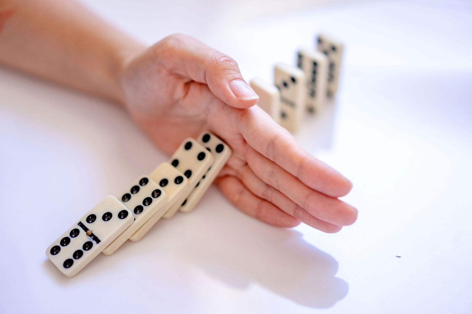 Hand stopping a row of falling dominoes.