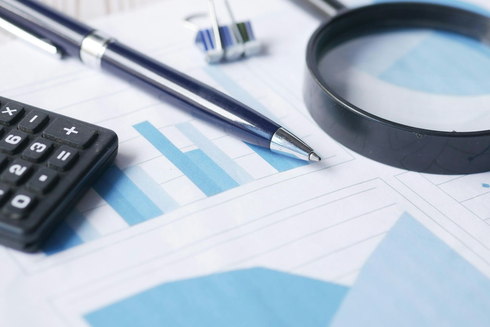 Calculator, pen, magnifying glass, and financial charts on a desk