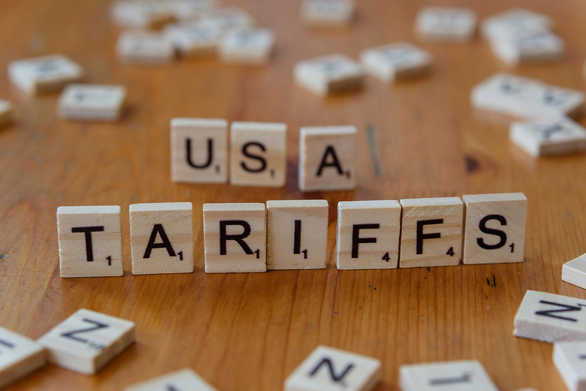 The word tariffs is written in scrabble tiles on a wooden table.