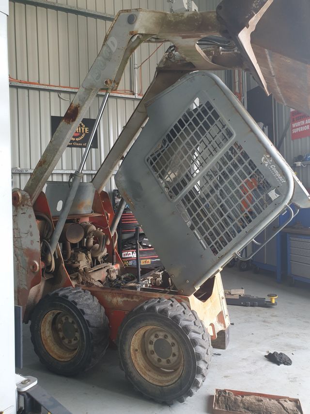 A skid steer is being repaired in a garage.
