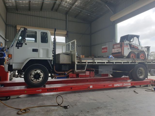 A white truck with a skid steer on the back is parked in a garage.