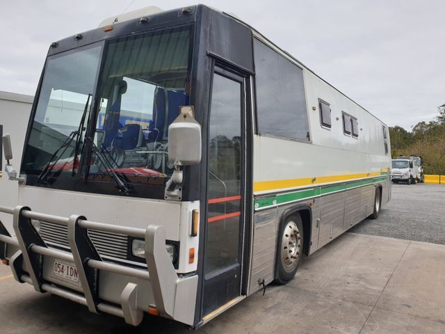 A white bus with a yellow stripe on the side is parked in a parking lot