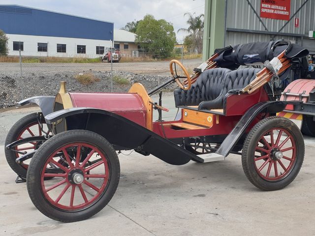 An old red and black car is parked in front of a building