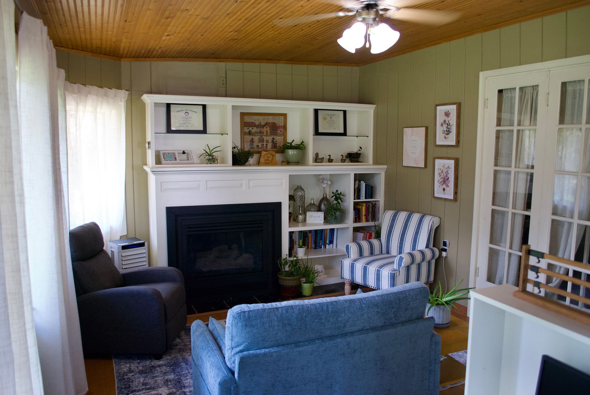 Cozy living room with fireplace, white built-ins, and blue seating. Light green walls, wood ceiling.