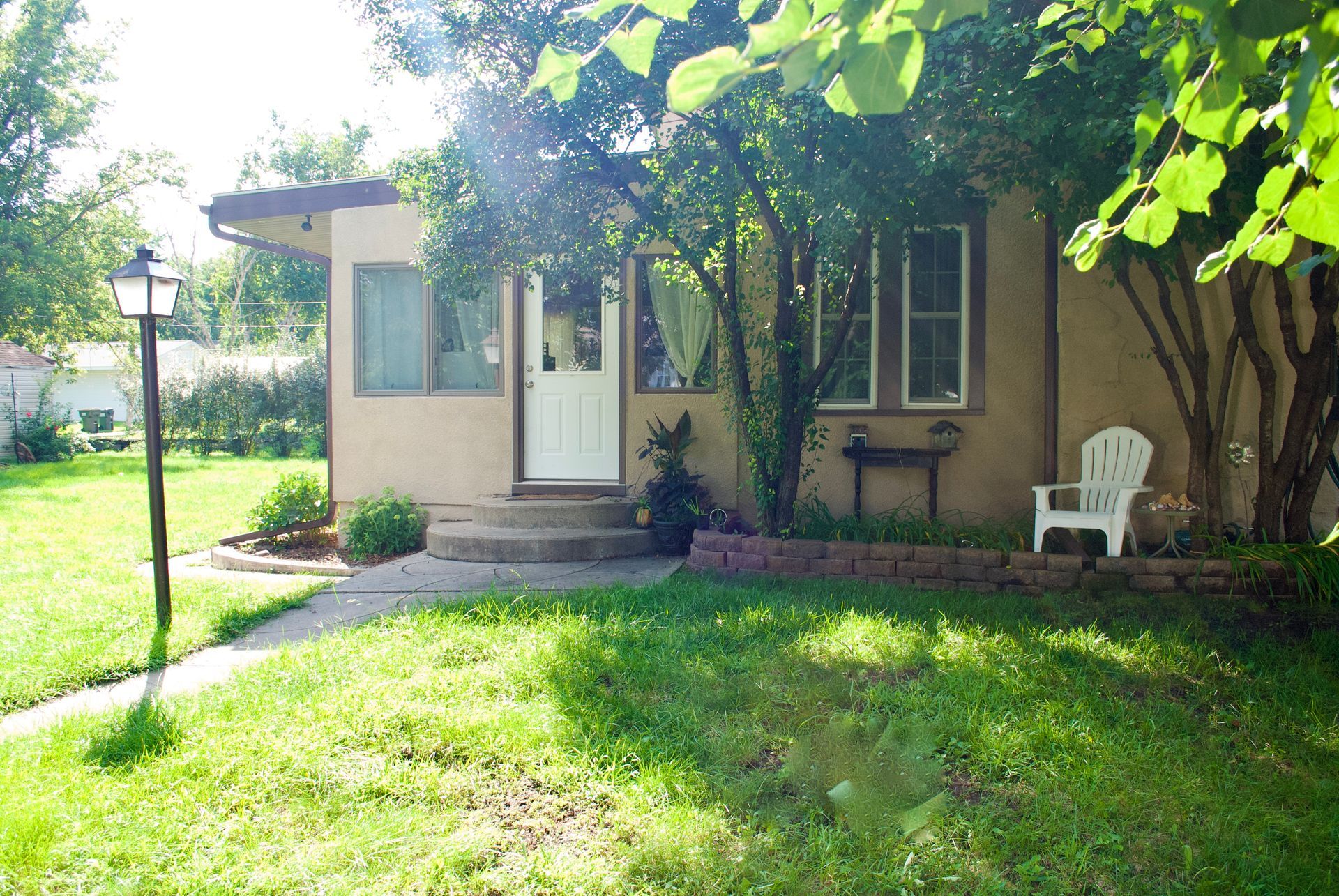 Tan house with a white door and small porch. A lamppost stands in the green lawn.