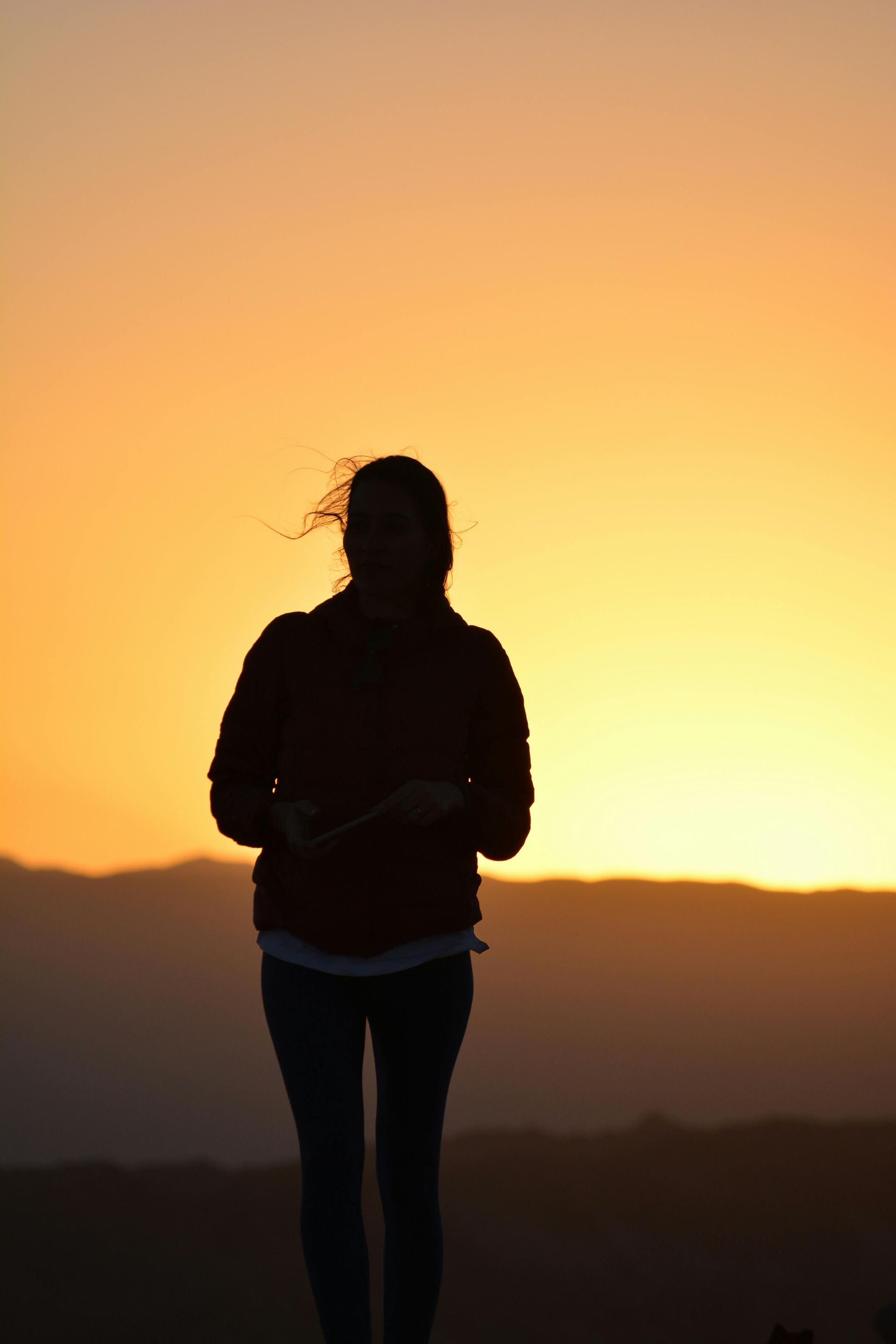 Silhouette of a person standing at sunset; orange sky, mountains in the distance.