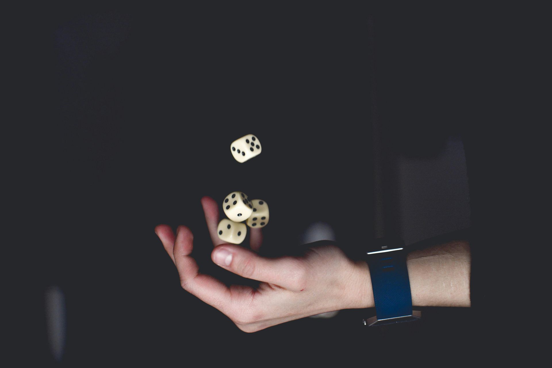Hand tossing four dice against a dark background.