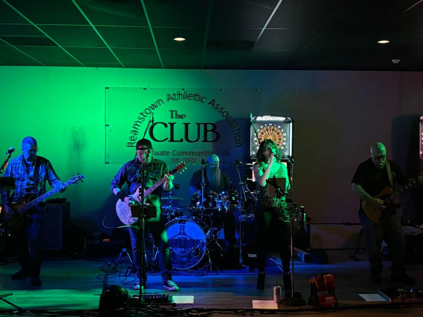 A group of people are playing instruments on a stage in front of a sign that says the club.