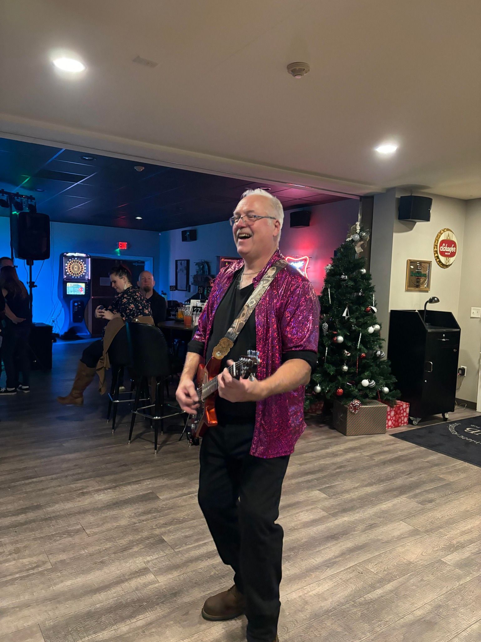 A man in a purple shirt is playing a guitar in a room with a christmas tree.