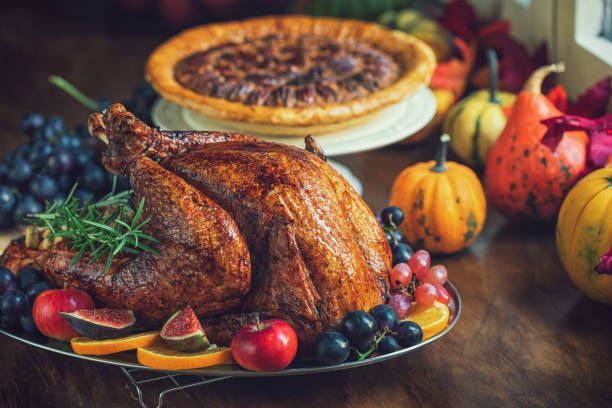 Thanksgiving feast with a roasted turkey, fresh fruit garnish, pecan pie, and festive pumpkins.