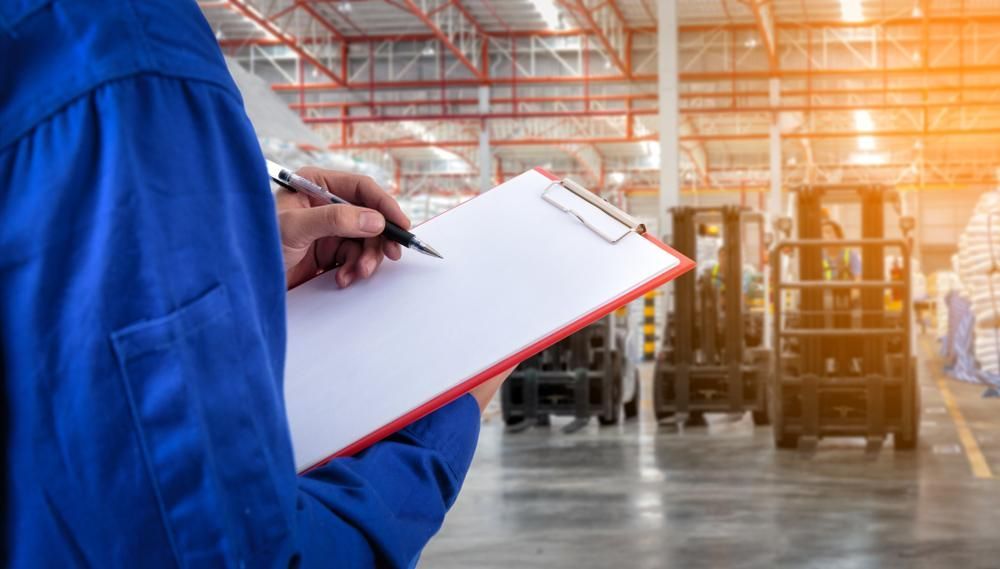 A Man Is Holding A Clipboard And Writing On It In A Warehouse — Adrians Mechanical Services In Warana, QLD