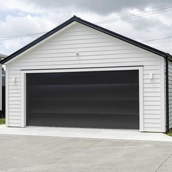 Typical double detached white garage with black tilt-up retractable raised panel metal door and gable metal roof