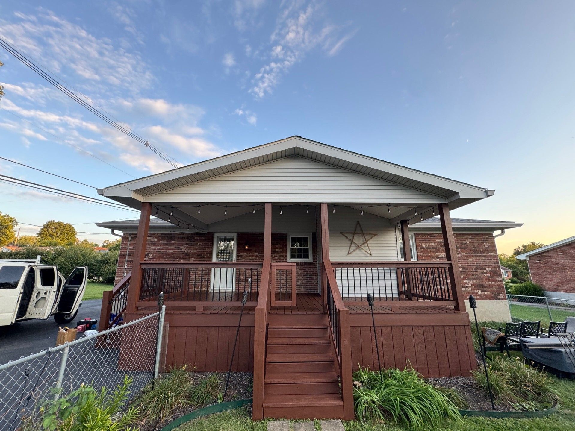 Brick house with a brown porch and stairs, string lights, blue sky.