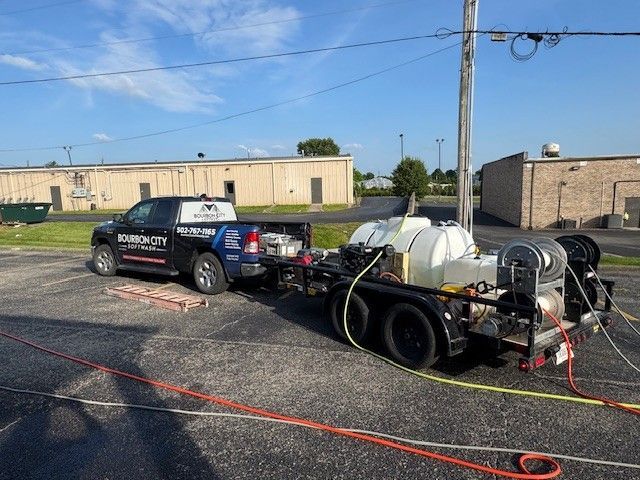 Truck with trailer, power washing equipment parked in a parking lot. Business logo on truck.