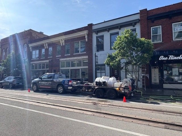 Truck and trailer parked on street in front of brick buildings, hoses and cones present.