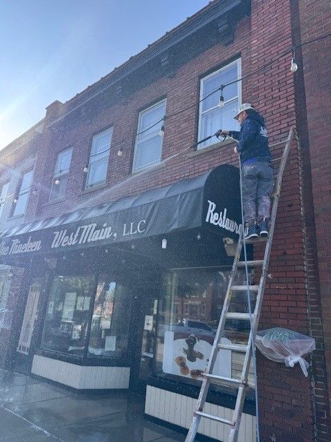 Person washing windows of a brick building with a restaurant awning.