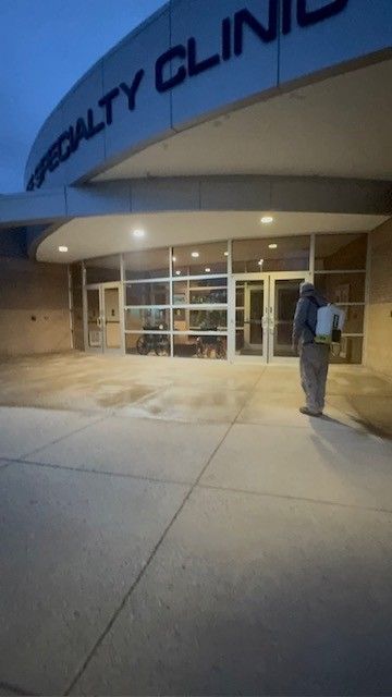 Person spraying disinfectant outside a specialty clinic building.