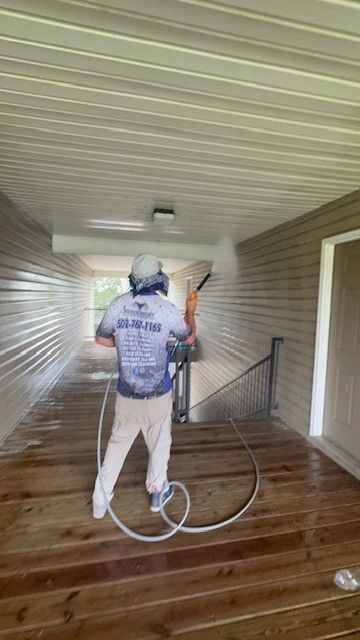 Man pressure washing a wooden porch, wearing protective gear.