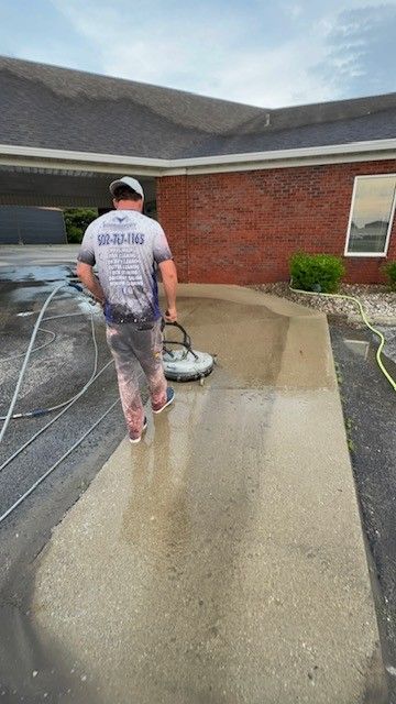 Man pressure washing a concrete sidewalk outside a brick building.